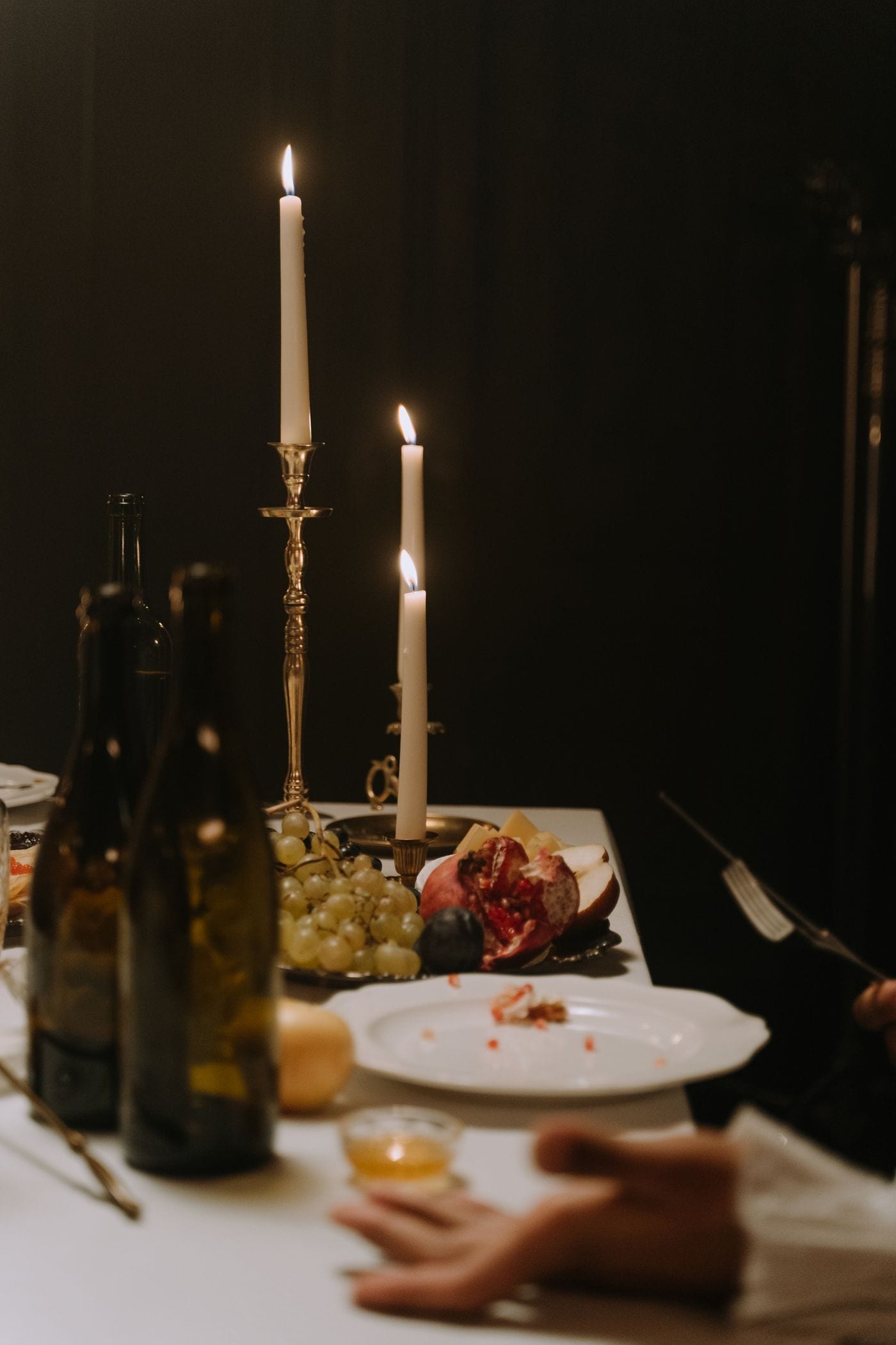 Brass candlesticks and dark bottles on a table lit only by candlelight