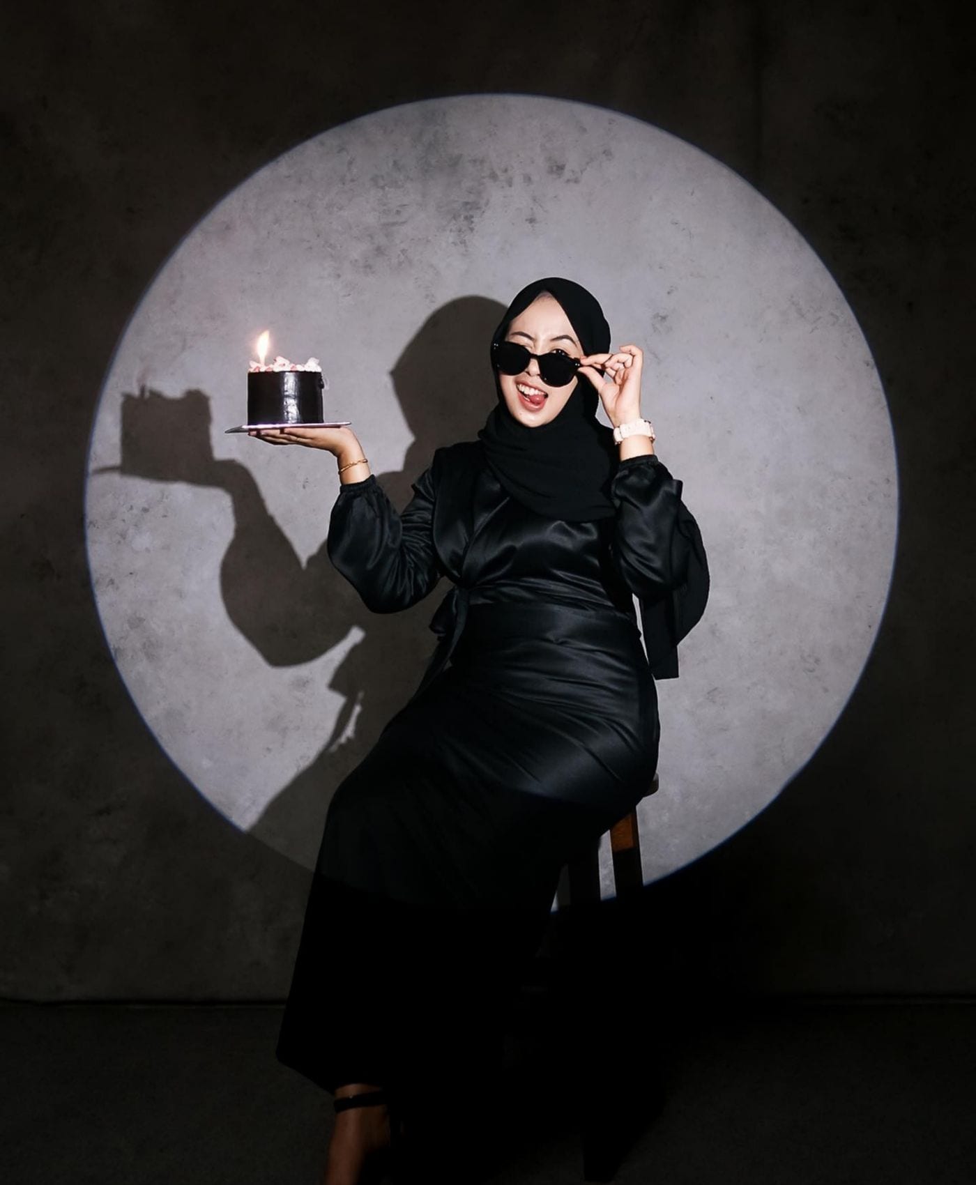 Guest in black holding a single-candle cake inside a circle of light