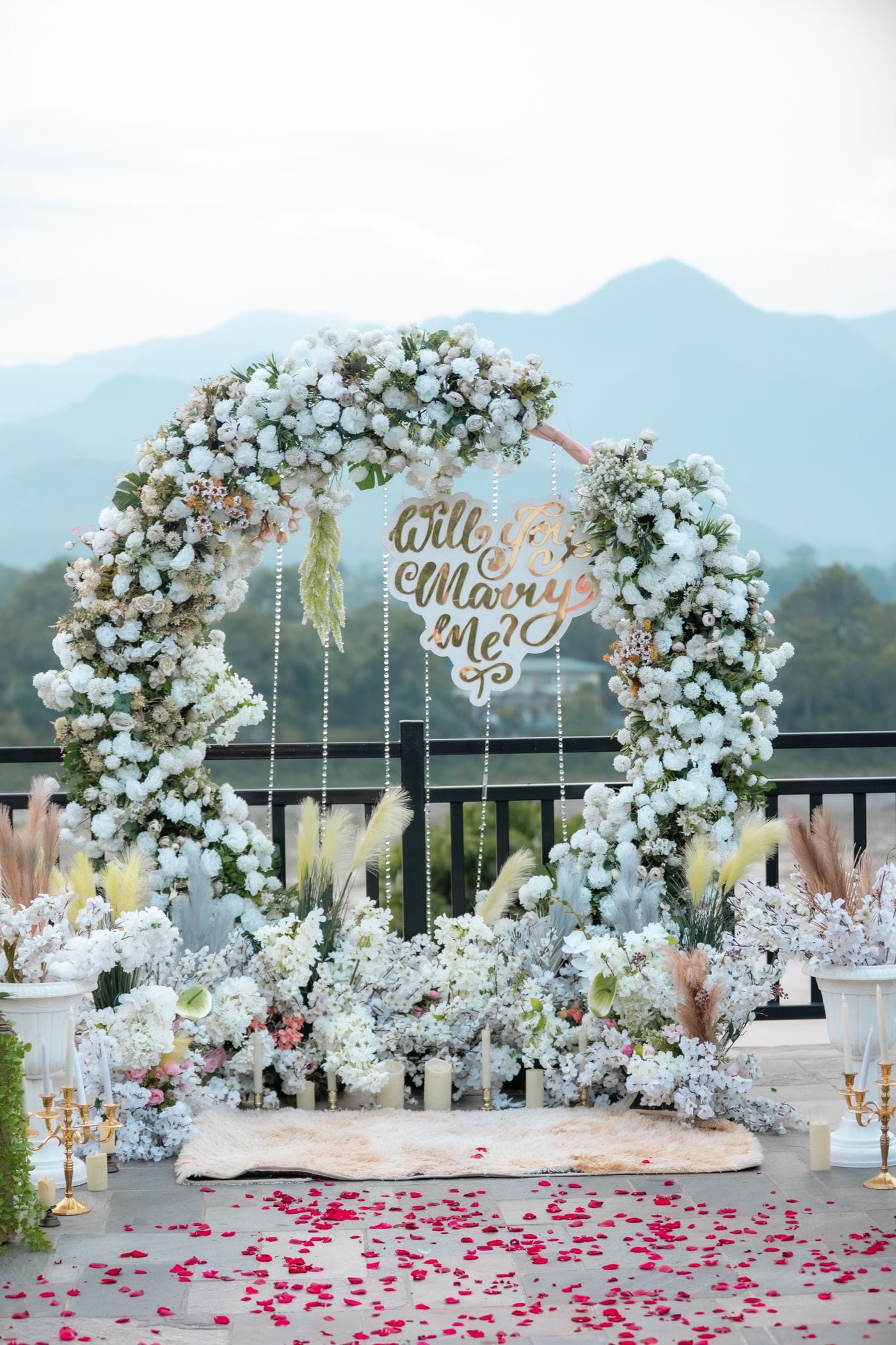 Floral arch with candles and rose petals on a terrace facing misty mountains